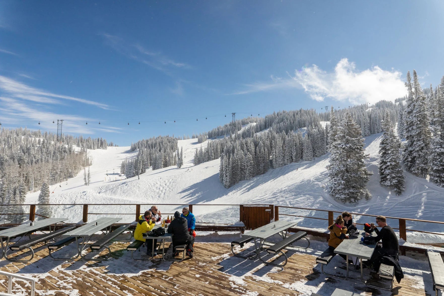 People sitting on the deck of Bonnie's Restaurant snowy mountain landscape and gondola in the background